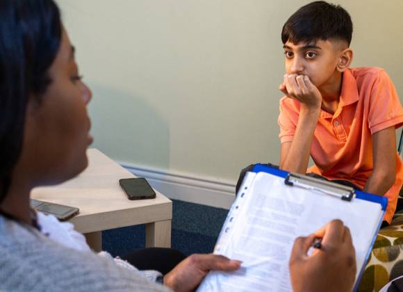 Professional person meeting with young person and taking notes using paper and clipboard.